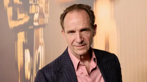 Getty Images Ralph Fiennes in a suit and pink shirt