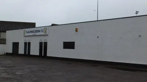 Alpin Stewart/Geograph A white wall of the outside of Clachnacuddin's Grant Street Park. There gates into the ground and sign that reads: "Clachnacuddin FC".