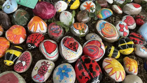 Multicoloured pebbles surround a tree in the garden, many decorated with Spiderman pictures which Elias loved.