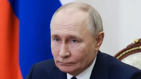 Reuters Russian President Vladimir Putin, whose head and shoulders are pictured, wears a navy suit as he chairs a meeting with members of the Security Council via video link at the Kremlin in Moscow. A Russian flag is visible behind him.