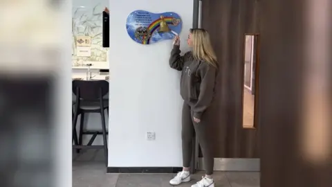 Holly Worswick A woman wearing an all brown outfit is ringing a rainbow bell to symbolise the end of her treatment. 