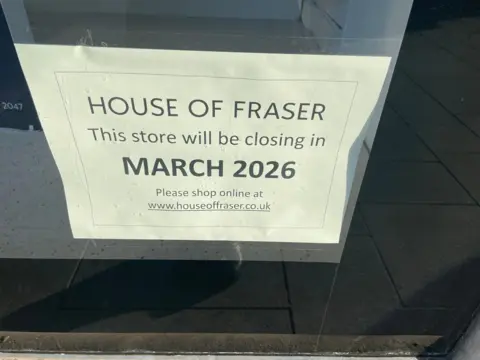 A picture of a poster in the window which reads "House of Fraser. This store will be closing in March 2026. Please shop online at www.houseoffraser.co.uk".  