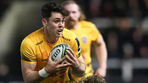 Oli Spencer with both hands wrapped around the ball to his chest, wearing Newcastle's yellow away kit