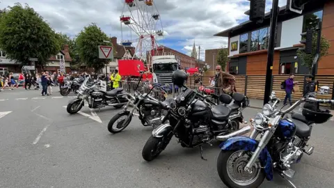 A row of motorbikes parked in front of a McDonald's branch on the right and a ferris wheel in the background.