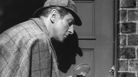 PA Media Black and white pic of Sherlock Holmes detective with a magnifying glass