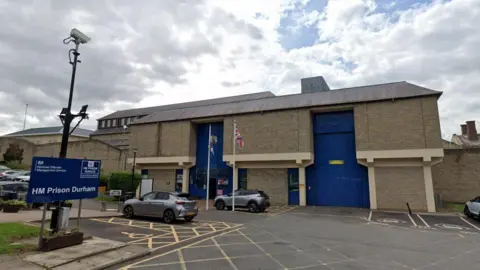 Googl Exterior of HMP Durham. It it is a large building made of light brown bricks with two giant blue doors in the wall's surface.