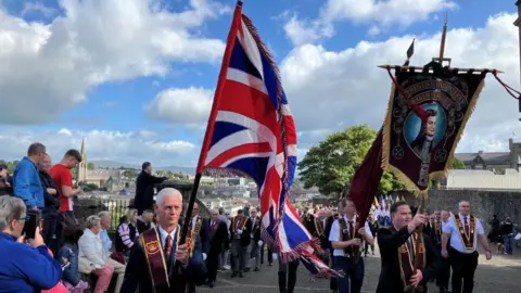 Loyal order members in uniform holding flags and banners