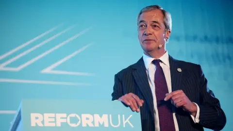 PA Media A politician in a suit. He is standing in front of a pale blue background. 