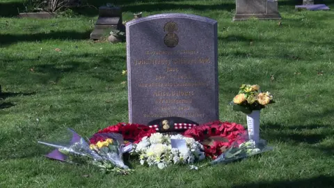 A gravestone at the cemetery with flowers laid next to it.