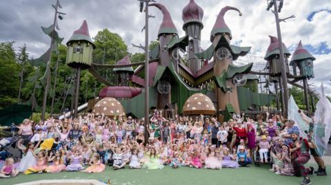 Dozens of children and adults dressed as fairies in front of a large and colourful play area