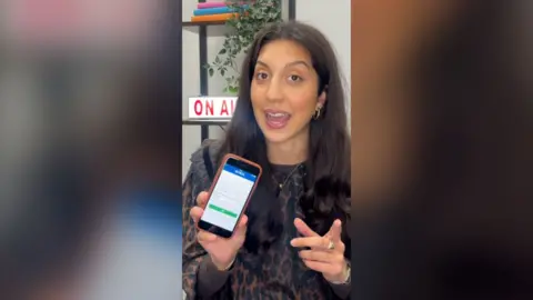 A woman with brown hair holds up an iPhone showing an app.