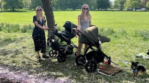 Julia Bryson/BBC Two women with blonde hair stand next to their pushchairs beneath cherry blossom trees on The Stray