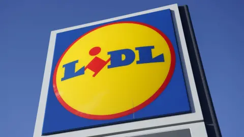 Lidl logo on a tall sign. It is a blue square, with a yellow circle outlined in red. The word Lidl is written in blue font and the I is red.