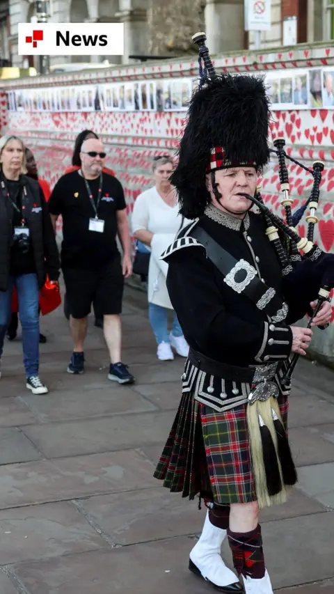 A man plays the bagpipes near the National Covid Memorial Wall on the COVID-19 Day of Reflection