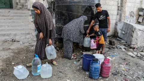 A group of Gazans including a man, two women and a child fill gallon bottles with water from a black water tank on the side of a street in Khan Younis in Gaza on 21 May.