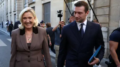 Reuters a smile Marine Le Pen and Jordan Bardella walk in the street