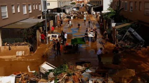 Reuters People clear a mud-covered street after heavy rain in Alfafar, Valencia