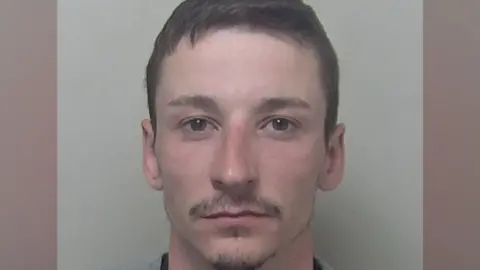 A custody photograph of Jamie Sutton shows a person with short dark hair looking directly at the camera against a plain light-coloured background.