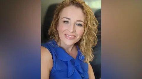 Supplied Julie Gorman Cliff is smiling at the camera as she takes a selfie. Her curly blonde hair reaches her shoulders. She has blue eyes and is wearing a blue sleeveless top. 
