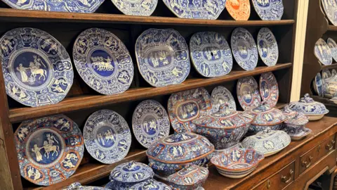 A display of blue-and-white decorative plates, bowls and serving dishes arranged on a large wooden cabinet.