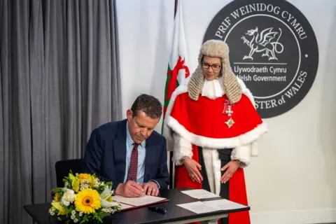 Matthew Horwood/Welsh government Rhun ap Iorwerth signs a document while being overseen by a judge.