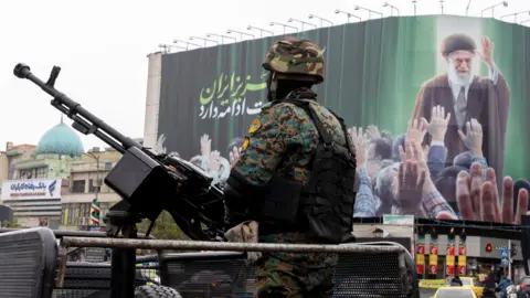 A police officer stands guard beneath a poster of Iran's former leader, Ayatollah Ali Khamenei on March 10, 2026 in Tehran, Iran. 