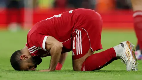 Mohamed Salah kneels on the pitch and touches his head to the ground in prayer after scoring.