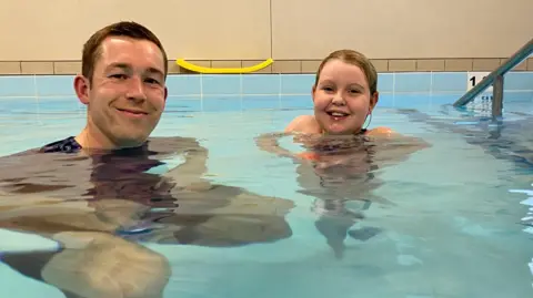 Alex Johnson who co-founded Nova sports sits in the pool with a student, both smiling into the camera