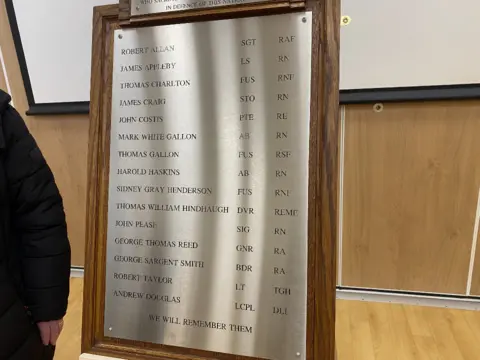 The names of men who sacrificed their lives during World War II from the village of Burradon visible on a silver plaque to commemorate each one of them. The names are engraved in black ink. The plaque has a wooden surround.