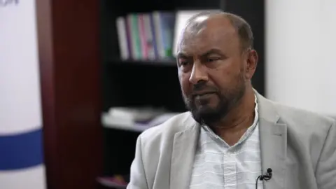 Dilowar Khan in a white shirt and grey suit jacket. 