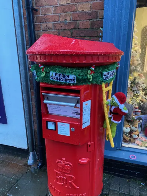 Syston Town News Postbox with knitted Grinch decorations below its top.
