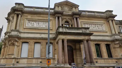 A photo of the exterior of a two-storey Victorian building which has a sign saying 'art gallery on it'. The building has marble pillars.