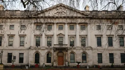 Reuters The exterior of a large white-walled building that was originally the site of the Royal Mint Court. At its centre is Palladian architecture, with columns built into the side, with an ornate triangular gable above.