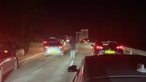 BBC Cars stopped on a motorway with people standing outside their cars, at night