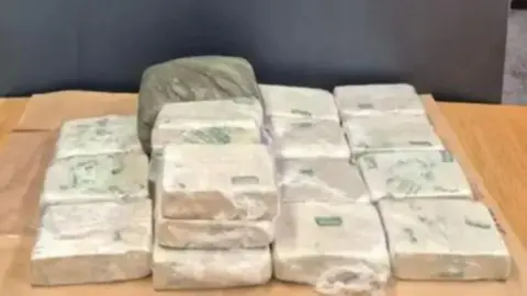 A wooden table with plastic wrapped blocks of drugs sitting on top of it.