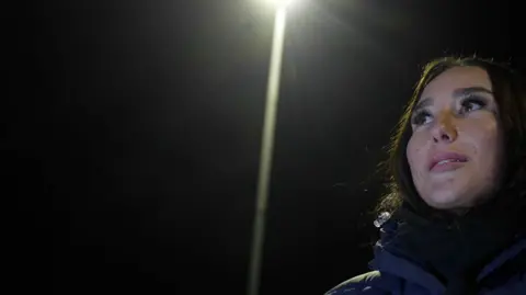 Jamie Niblock/BBC Connolly-Brame looks out onto the training pitch, illuminated by the floodlights on a cold winter's evening. Her breath visible. 