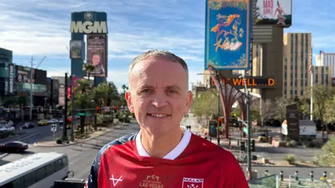 Simon Latus Simon Latus standing in front of the MGM Hotel. He has short brown hair and is wearing a red HKR shop