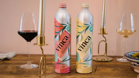 Vinca Two wine bottles made with aluminium stand next to a glass of red wine