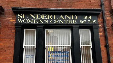 Black shop front of brown brick wall which says in gold lettering: Sunderland Women's Centre. 