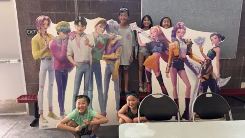 Supplied Children posing around large cut-outs of characters from K-pop Demon Hunters
