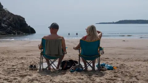Two people on chair sitting on a beach. They are looking out at the sea. 
