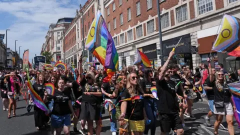 PA Media A group of people waving rainbow LGBTQ+ flags.