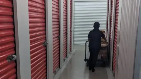 Apple Storage A lady pushes a trolley down the aisle of a self-storage facility