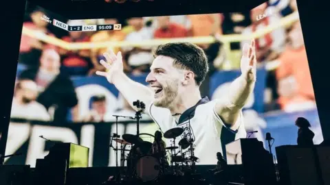 Chris Phelps The moments after the final whistle was blown at England's semi-final is shown on a big screen behind the band on stage