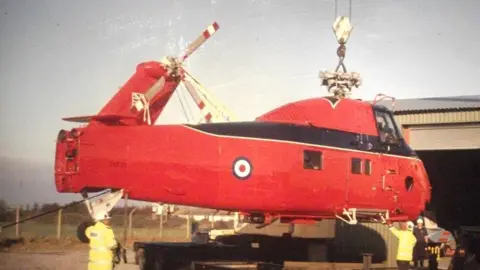 The Helicopter Museum A red helicopter being lowered by a crane in the open air