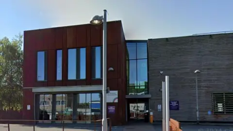 The front of a large red-brown coloured building with tall windows