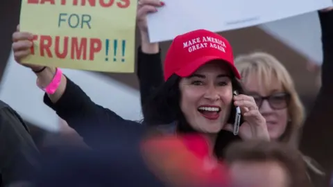 Woman wearing MAGA hat and holding sign saying 'LATINOS FOR TRUMP'