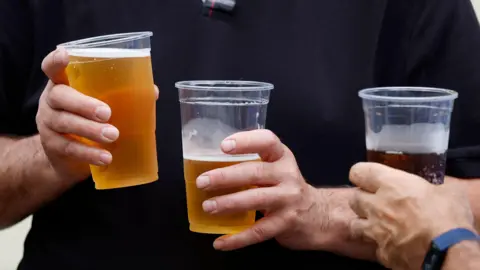 Three cups of beverages including two cups of beer being held. 