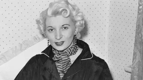 Bettmann Archive/Getty Images Ruth Ellis in black and white photo taken before her arrest wearing striped scraf and dark collared jacket, long earrings and she has short blonde hair. 