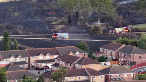 housing estate in front of burnt grass land, with fire engines